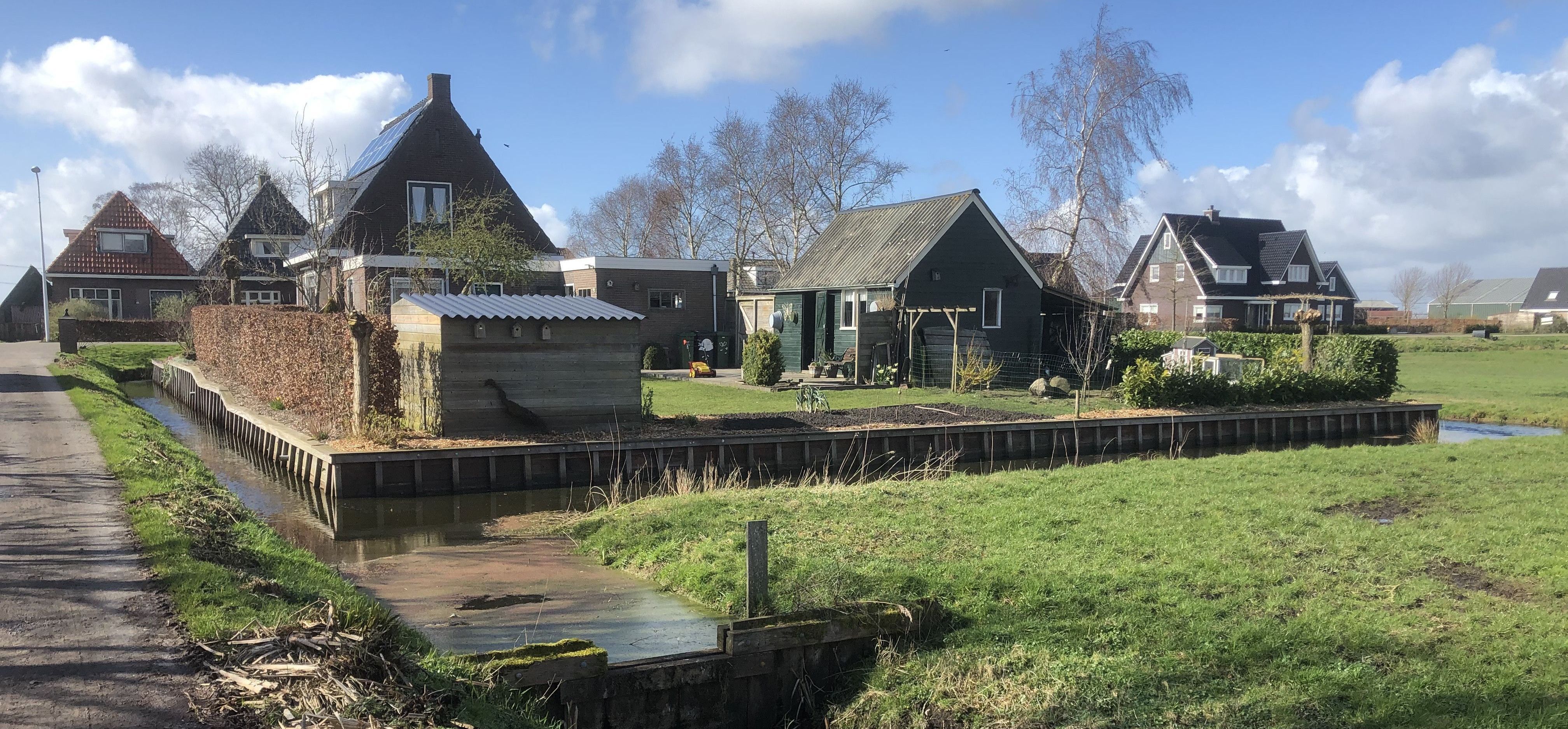 Foto van rij met woningen aan de achterzijde met een hoogwatervoorziening erbij