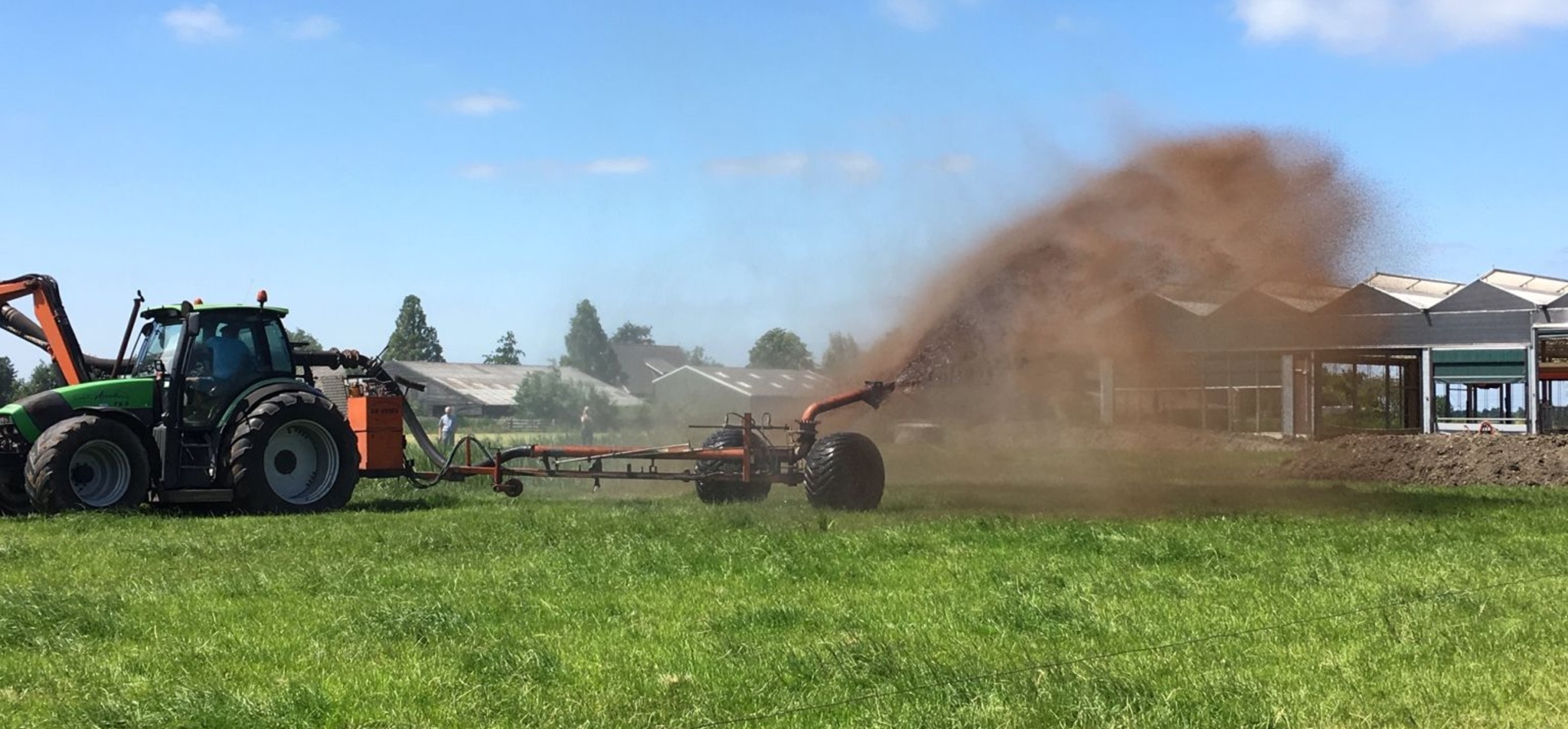 Foto van een tractor die klei over een weiland verspreidt met een ruwe mestverspreider